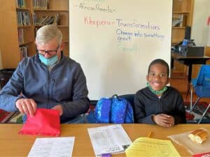 Carl Anderson provides homework tutoring to a smiling young student.